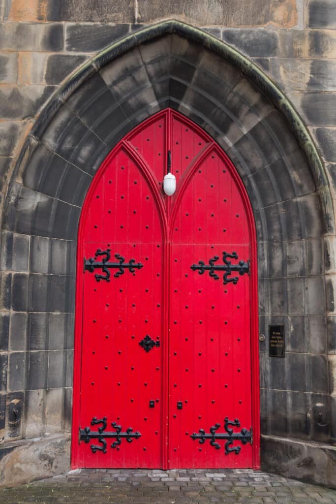Red big wooden door with metal black parts on a stone building in Edinburgh Scotland
