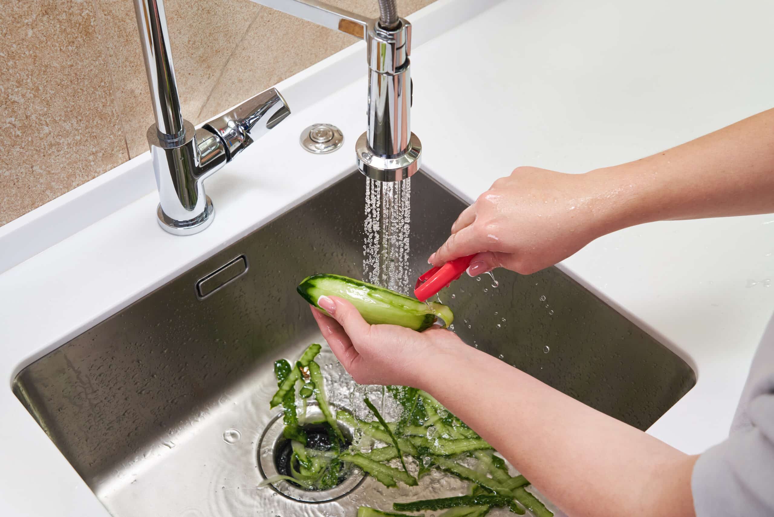 Female hands peeling cucumber over food waste disposer