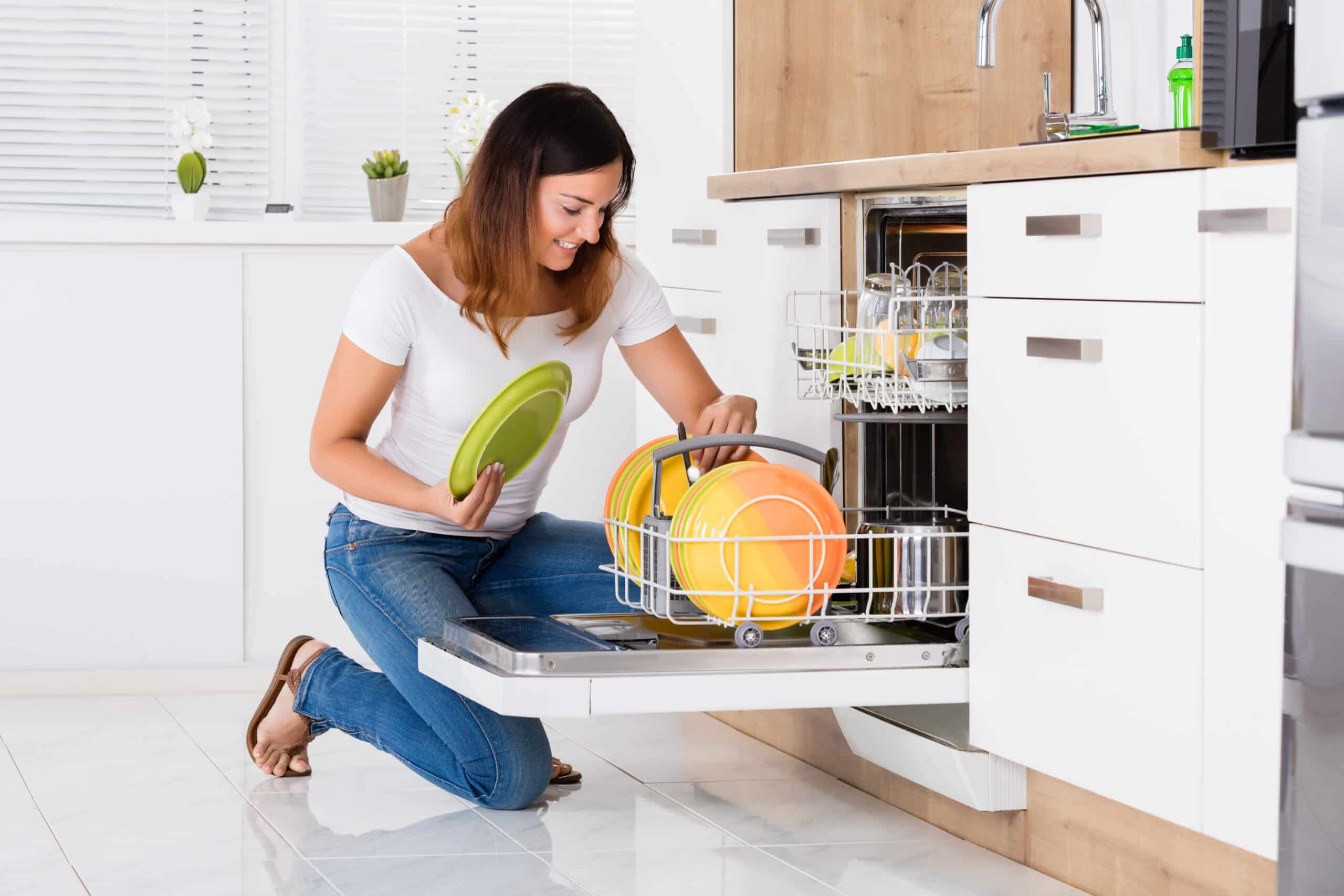 A woman kneeling in front of a dishwasher